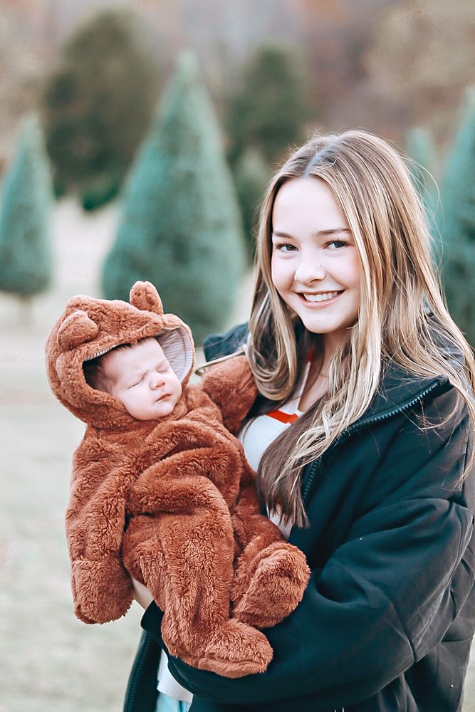 Baby in a bear suit with her sister at a Christmas tree farm