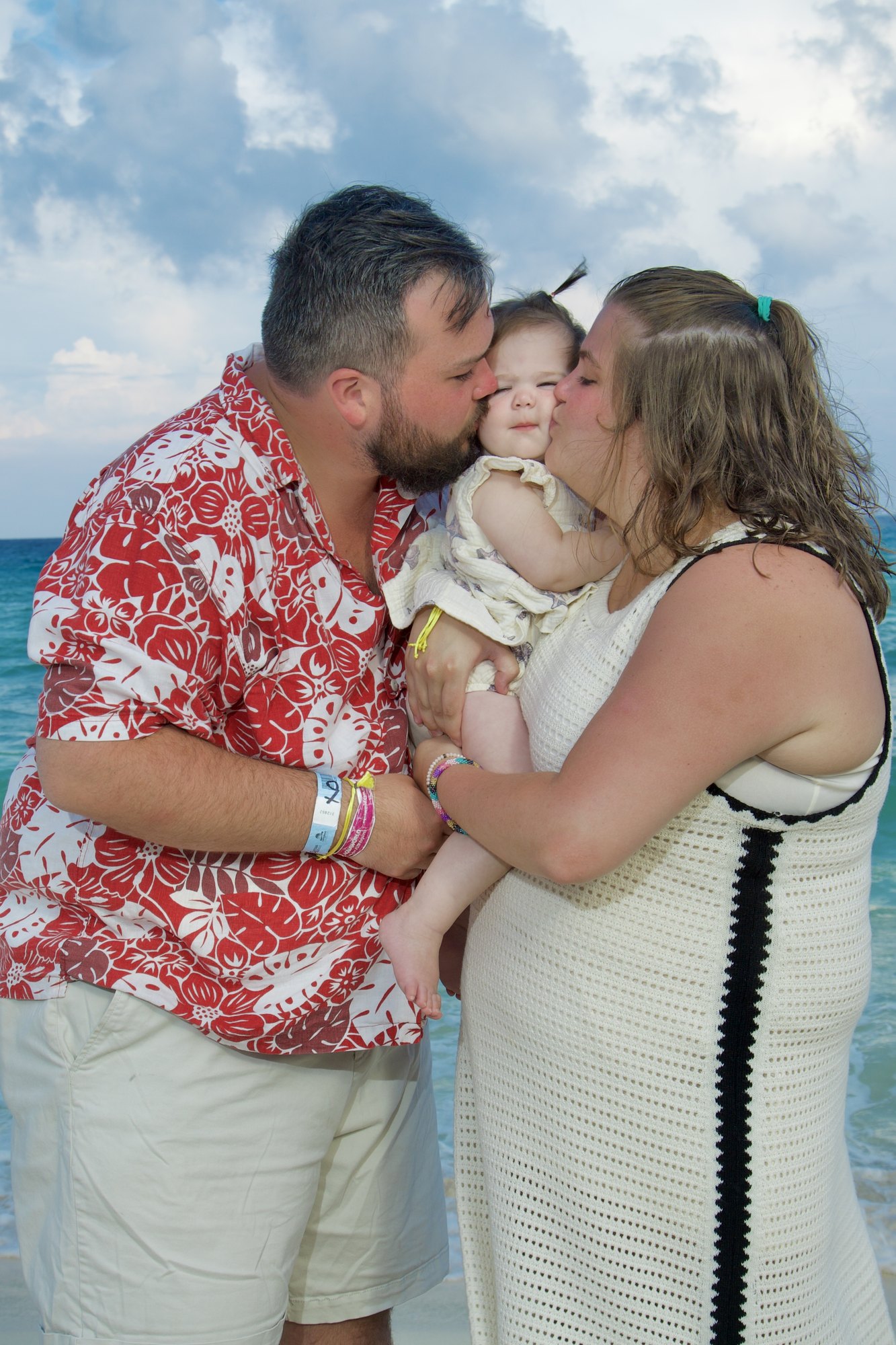 Family sharing a kiss with their baby girl on the beach