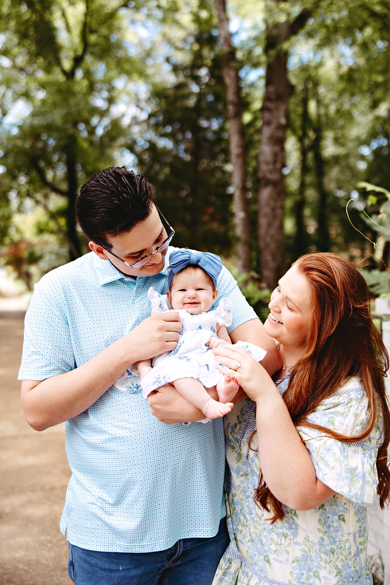 Young family holding their baby girl under the trees